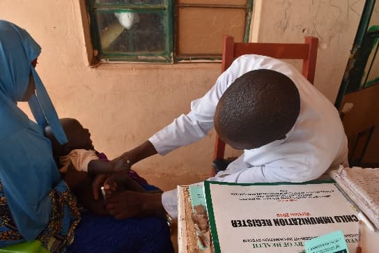 Health worker vaccinating a baby beside a child immunisation register